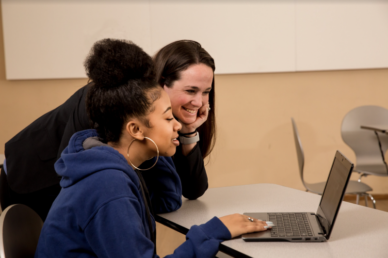 A teacher and student looking at a computer screen and smiling. 