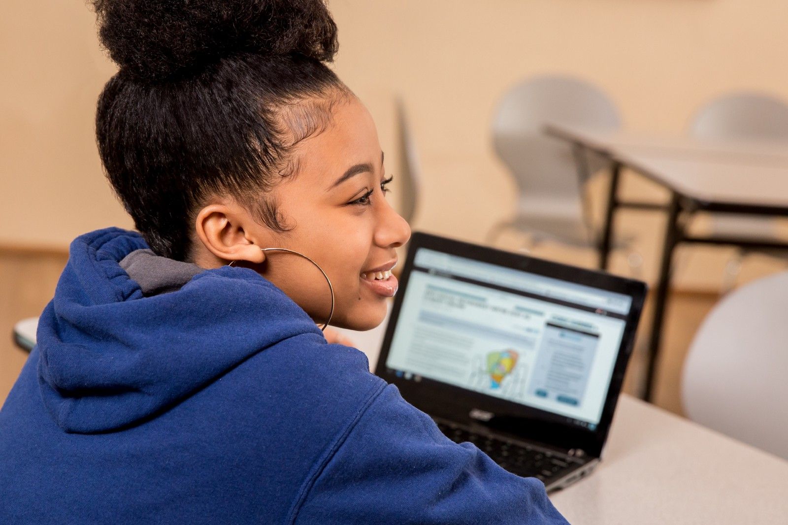 A student working on a CommonLit lesson on her computer and smiling. 