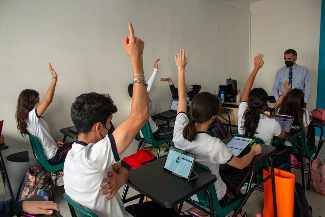 Students with hands raised in a classroom in Mexico