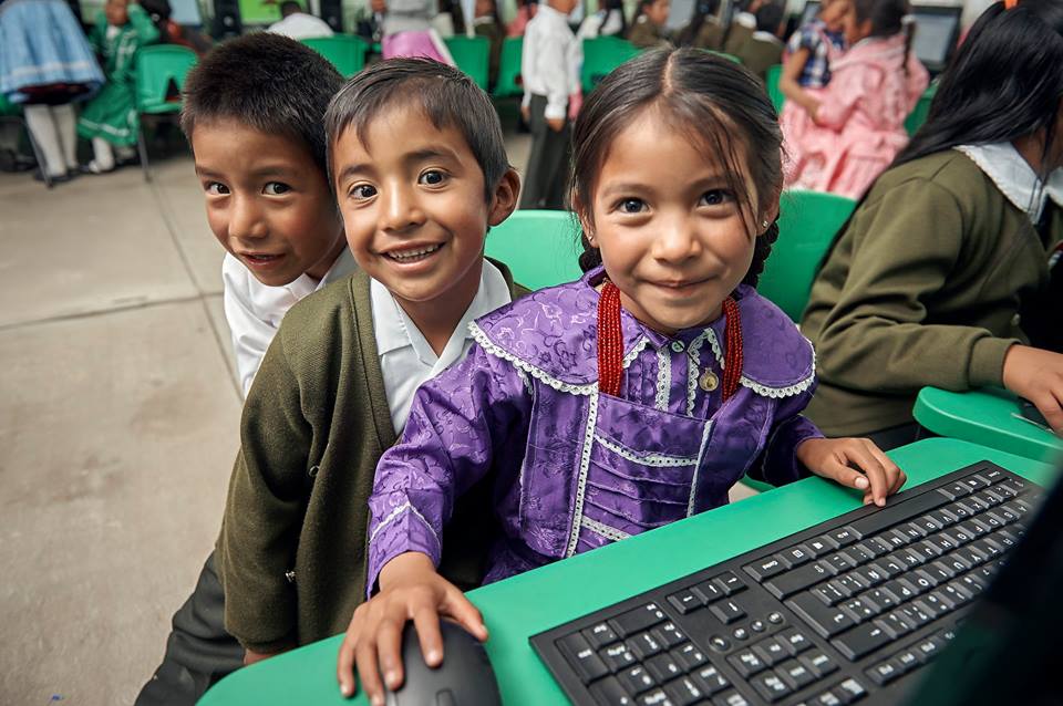 Tres niños sonriendo en frente de una computadora