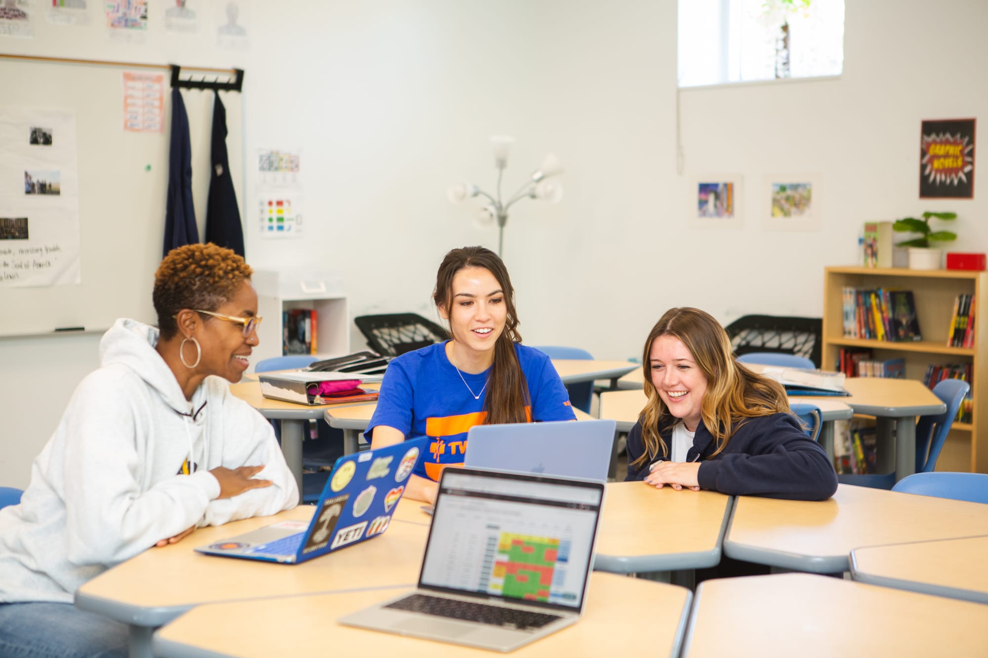 Three smiling female teachers looking at data on laptops